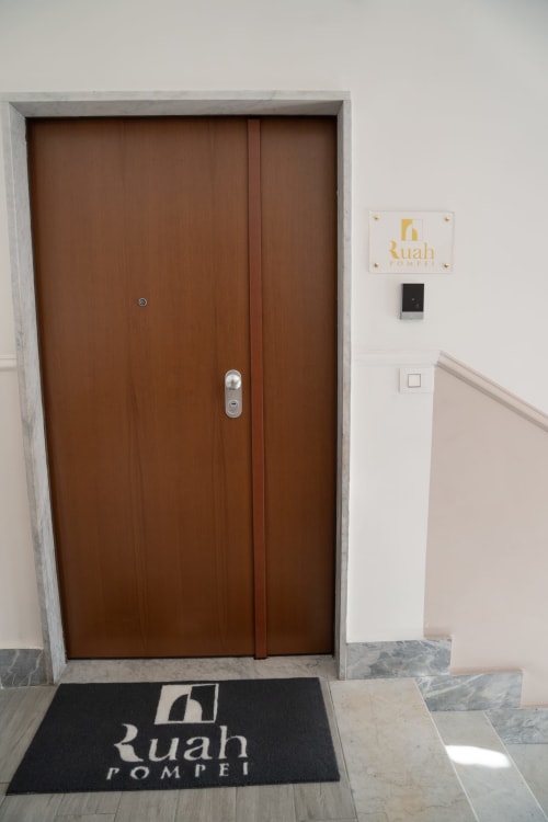 Ingresso con porta in legno scuro presso la struttura Ruah Pompei a Pompei, con zerbino personalizzato
