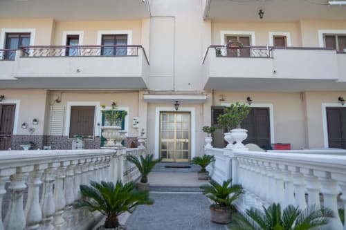 Cortile della Ruah Pompei B&B con balaustre bianche, piante di palma e porta centrale gialla a Pompei, Italia