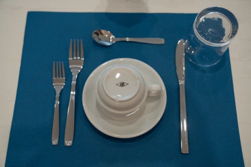 Tavolo formale presso il bed and breakfast Ruah Pompei a Pompeii con tovaglietta blu, stoviglie bianche, posate e bicchiere d'acqua