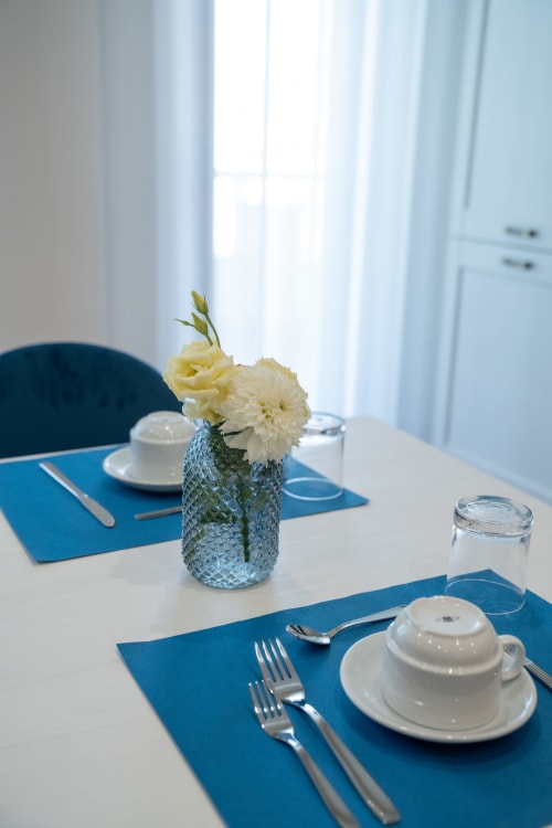 Elegante mise en place nella sala da pranzo di Ruah Pompei B&B con fiori crema, tovagliette blu e stoviglie bianche