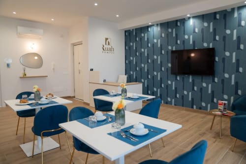 Sala da pranzo del Ruah Pompei B&B con sedie blu, tavoli bianchi, parete decorata, TV e arredi moderni a Pompei
