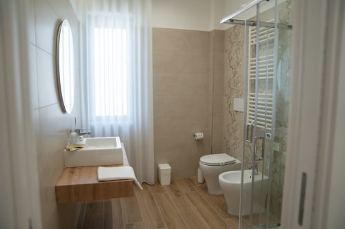 Modern bathroom at Ruah Pompei B&B in Pompeii with wooden flooring, vessel sink, toilet, and glass shower enclosure