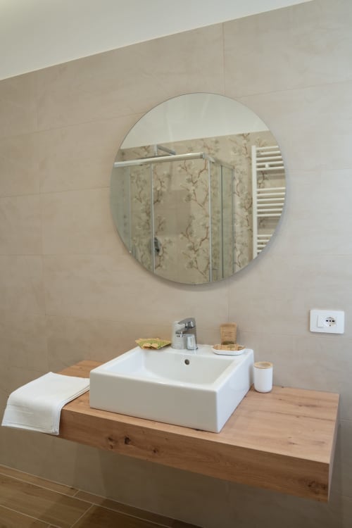Modern bathroom with round mirror and white vessel sink on wooden counter at Ruah Pompei B&B in Pompeii, Italy