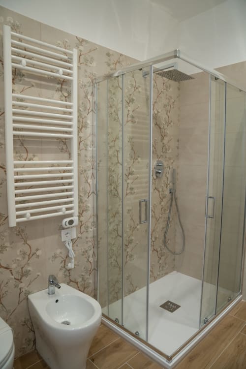 Modern bathroom with walk-in shower, white heated towel rail, and botanical tile pattern at Ruah Pompei, Pompeii