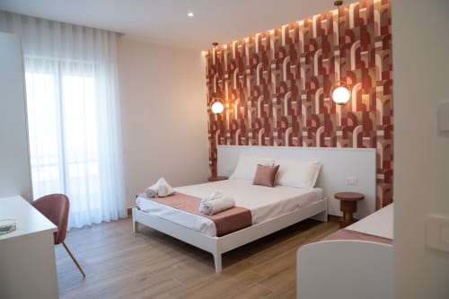Modern triple bedroom at Ruah Pompei B&B in Pompei with geometric patterned accent wall, white bed, and city balcony view