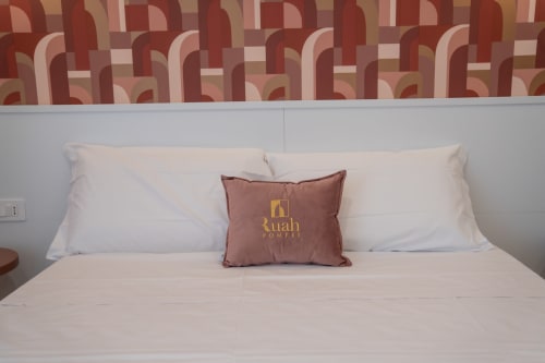 Camera d'hotel Ruah Pompei con cuscini bianchi, cuscino decorativo bordeaux con logo, testata rossa a motivi e biancheria beige