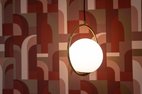 Modern pendant light with brass ring and frosted globe in Ruah Pompei hotel room with geometric patterned wallpaper