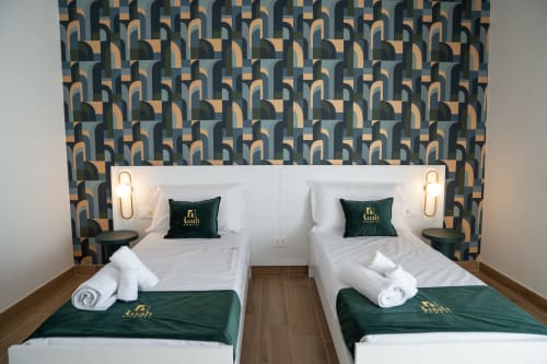 Twin beds in green-accented room at Ruah Pompei hotel, Pompeii, with geometric patterned headboard and gold sconces