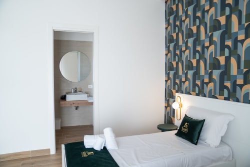 Ruah Pompei double room with circular mirror, geometric wallpaper, white bedding, and ensuite bathroom view