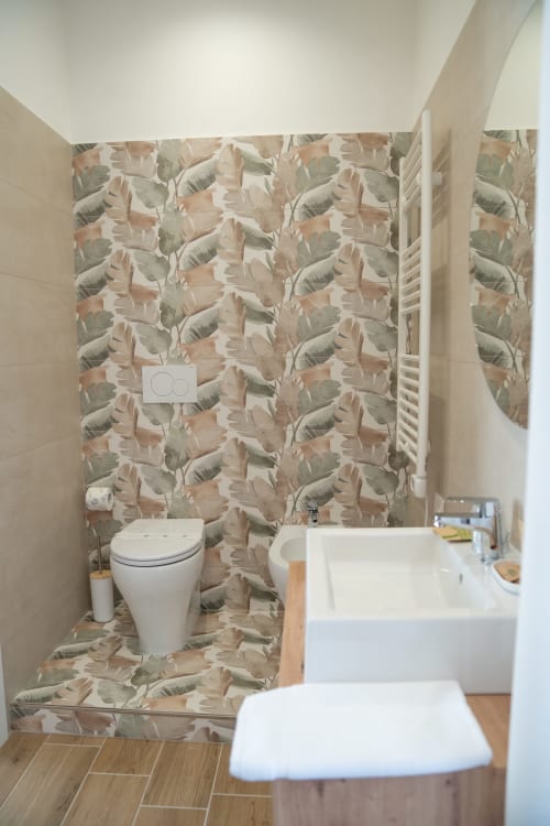 Modern bathroom at Ruah Pompei B&B in Pompei with botanical wallpaper, white toilet, sink, and wooden flooring
