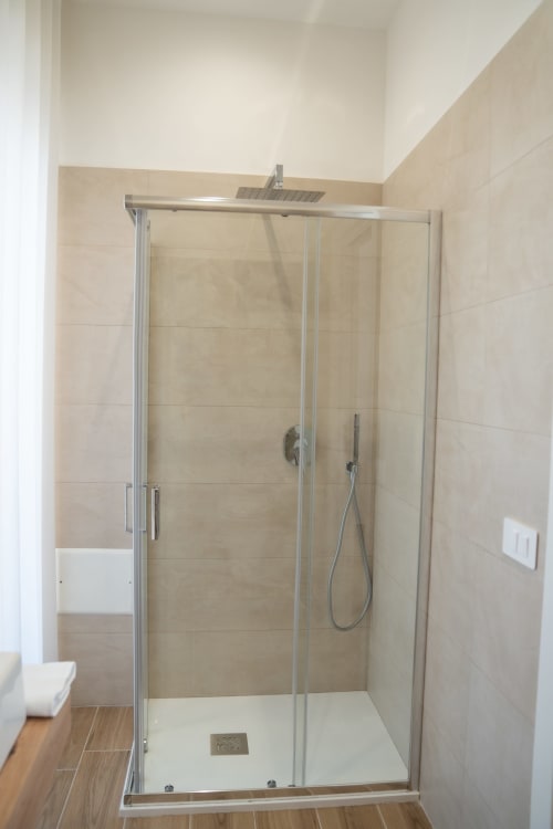 Modern shower enclosure with rainfall showerhead at Ruah Pompei hotel in Pompei, featuring beige tile walls and glass doors