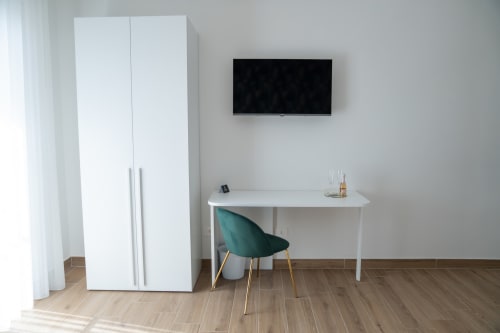 Modern hotel room at Ruah Pompei with white desk, green chair, wall-mounted TV, wardrobe, and wooden flooring