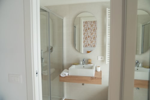 Modern bathroom at Ruah Pompei B&B in Pompeii with white vessel sink, oval mirror, shower, and wooden vanity
