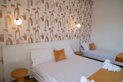 Bright triple bedroom at Ruah Pompei B&B in Pompeii with geometric patterned wallpaper, white beds, gold accents, and pendant
