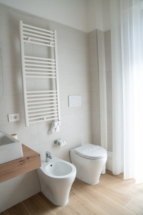 Modern bathroom at Ruah Pompei B&B in Pompei with white fixtures, heated towel rack, bidet, toilet, and wooden vanity