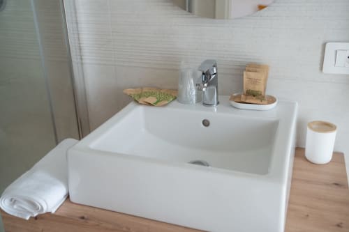 Modern white bathroom sink with chrome faucet, wooden accents, and eco-friendly toiletries at Ruah Pompei B&B in Pompei,