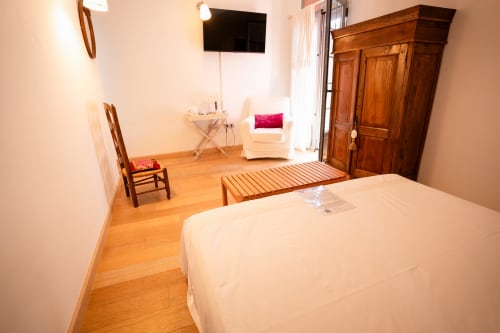 Espaciosa habitación doble en Casa Rural La Perla con suelo de madera, cama blanca, TV, sillón y armario