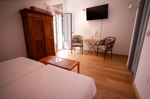 Spacious twin room at Casa Rural La Perla with wooden wardrobe, two patterned chairs, flat-screen TV, and garden view balcony