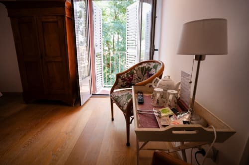 Cozy room with wooden chair, desk, floor lamp, and open balcony doors overlooking gardens at Casa Rural La Perla