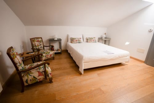 Chambre double spacieuse à Casa Rural La Perla avec plancher en bois, lit blanc, fauteuils fleuris et équipements modernes