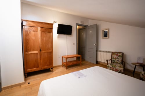 Spacieuse chambre double à Casa Rural La Perla avec armoire en bois, lit blanc, télévision écran plat et mobilier rustique