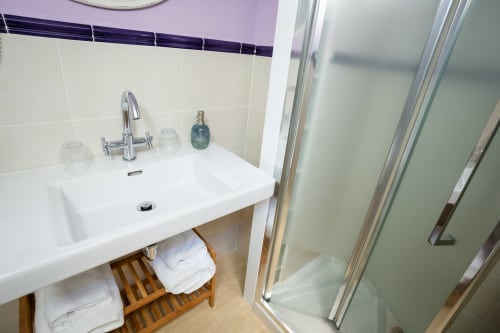 Salle de bain moderne de Casa Rural La Perla avec lavabo blanc, robinetterie chromée, étagère en bois et douche vitrée