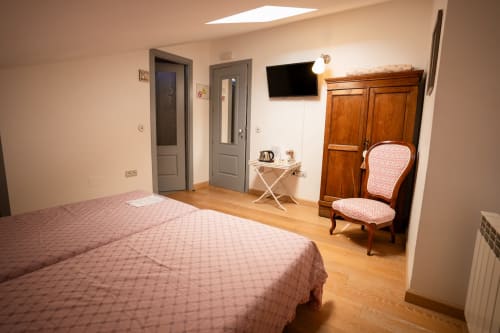 Chambre spacieuse de Casa Rural La Perla avec lit queen-size, armoire en bois, fauteuil rose et TV écran plat à Hiendelaencina