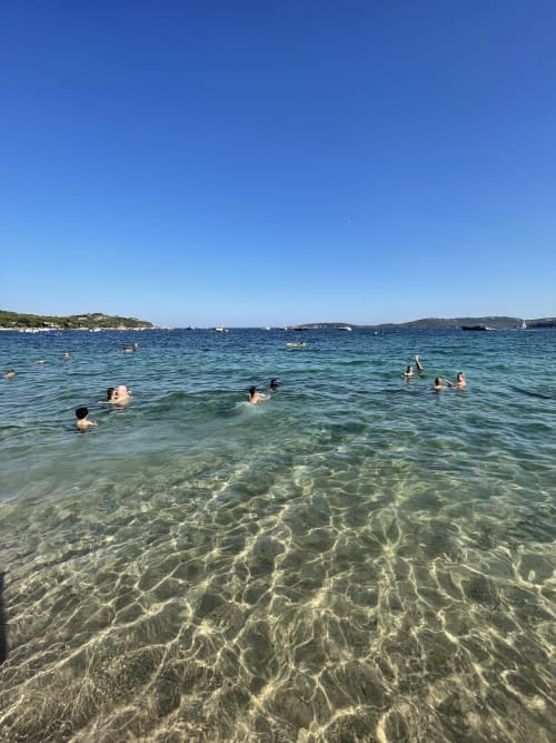 Acque turchesi cristalline con bagnanti sulla spiaggia sarda vicino a Varenna, punteggiata da barche e colline verdeggianti