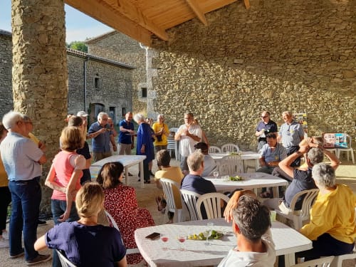 Guests gather at L'Amiradou guesthouse in Félines-sur-Rimandoule, enjoying wine and conversation in a stone courtyard.