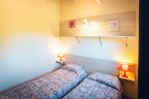 Chambre douillette de la villa Le Maquis Plage à Poggio-Mezzana avec lits jumeaux, éclairage chaleureux et étagère au-dessus de la tête de lit