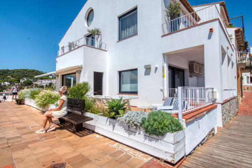 Modern white apartment building in Palafrugell with terracotta patio, guest seating, and hillside views under clear sky