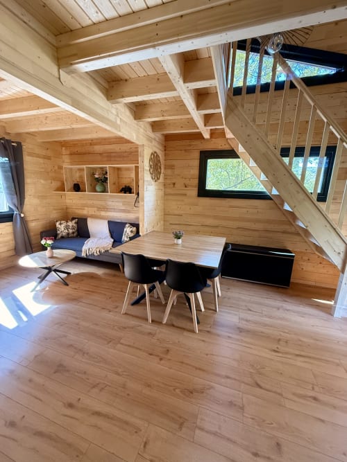 Interno di villa moderna in legno con tavolo da pranzo, angolo salotto e scala presso Cabanes et lodges du Belvédère, Serrières-sur-Ain
