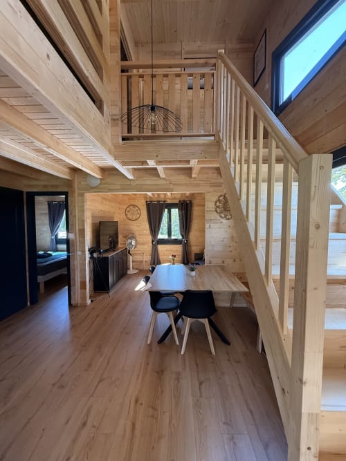 Interno di villa moderna in legno alle Cabanes du Belvédère con tavolo da pranzo, soppalco in mezzanino e vista lago a Serrières-sur-Ain