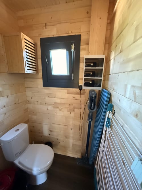 Bagno compatto in legno in villa con wc bianco, finestra con telaio scuro, ripiani e pareti in pino rustico presso Cabanes et lodges