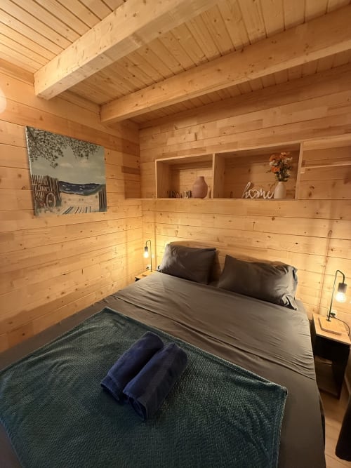 Accogliente camera da letto in legno con letto queen, biancheria grigia, scaffali incorporati, lampade a sospensione e travi in legno naturale