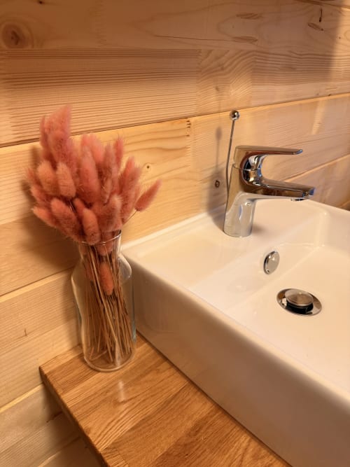 Lavabo da bagno moderno con rubinetteria cromata e decorazione con erba della pampa rosa nella villa Cabanes et lodges du Belvédère