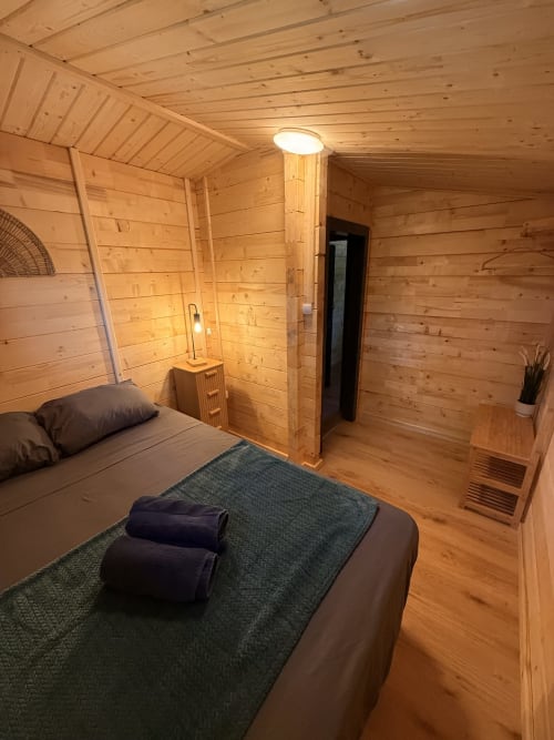 Accogliente camera in legno alle Cabanes et lodges du Belvédère con letto, coperta verde e illuminazione moderna