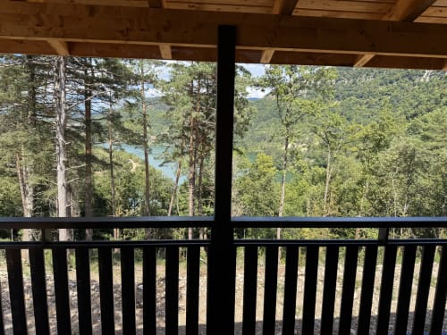 Terrazza in legno con ringhiera nera affacciata sulle montagne boscose e il lago presso Cabanes et lodges du Belvédère, Serrières-sur-Ain