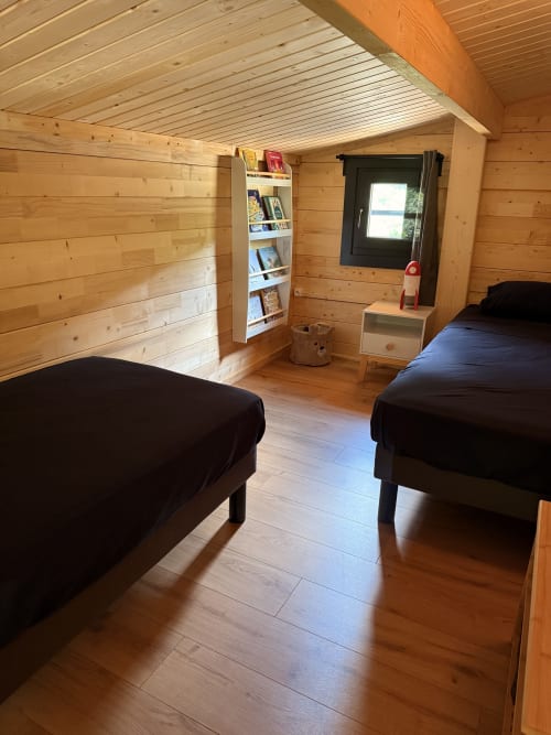 Camera da letto in legno con due letti, libreria e finestra presso Cabanes et lodges du Belvédère, Serrières-sur-Ain