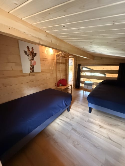 Accogliente camera da letto in villa di legno con due letti blu, opera d'arte giraffa e lucernario alle Cabanes du Belvédère a Serrières-sur-Ain