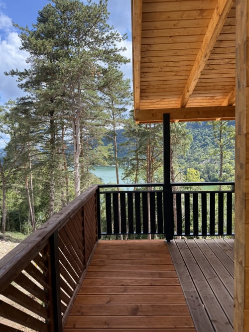 Terrazza in legno con balaustre nere che si affacciano sul lago di Serrières-sur-Ain e sulle montagne boscose, villa La Colibă