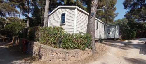 Mobil-home aux murs blancs au Camping La Lézardière à La Valette du Var, entouré de pins et de murs en pierre