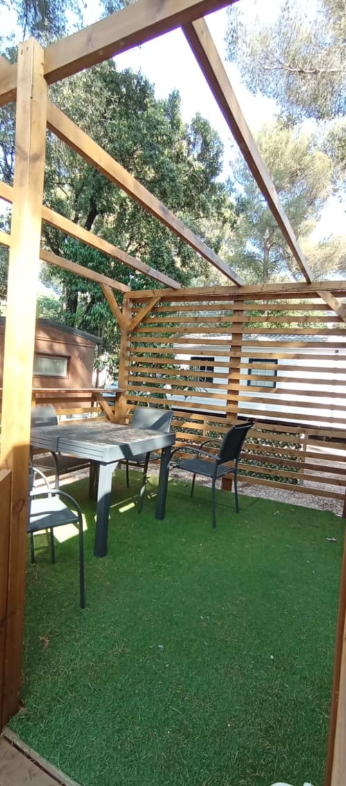 Pergola en bois avec table de salle à manger et chaises au Camping La Lézardière, La Valette du Var, entourée d'arbres
