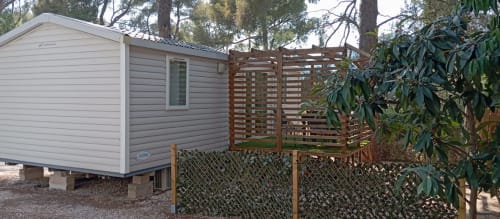 Mobil-home au Camping La Lézardière avec terrasse en bois et clôture ajourée, entouré d'arbres à La Valette du Var