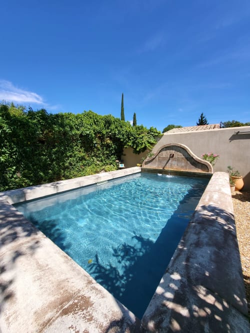 Piscine bleu cristal au Cabanon du Clos à L'Isle-sur-la-Sorgue, entourée de haies luxuriantes et d'architecture méditerranéenne