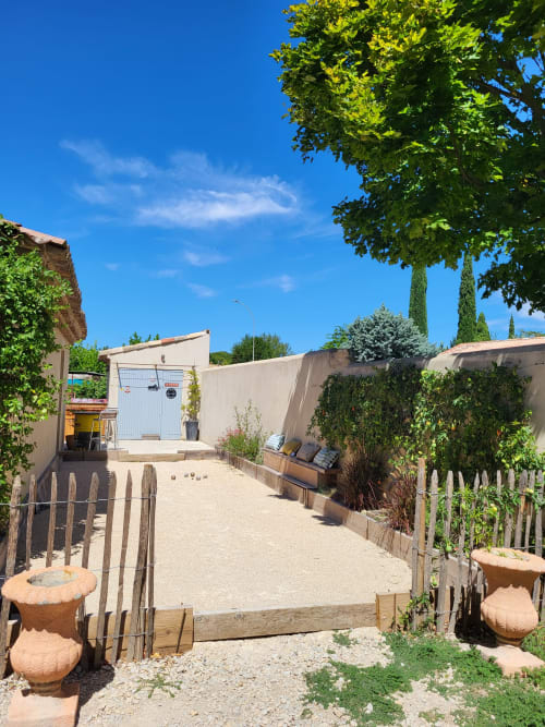 Cour ensoleillée du gîte Le Cabanon du Clos à Isle sur la Sorgue avec bancs et cyprès