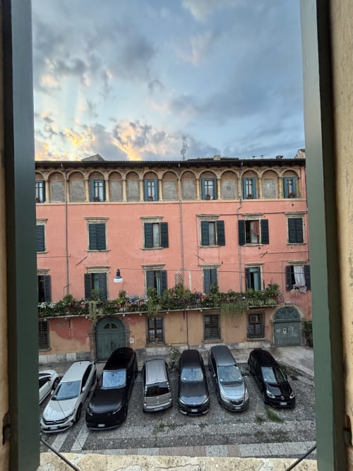 Edificio storico rosso con finestre ad arco che si affaccia su auto parcheggiate a Verona, Italia