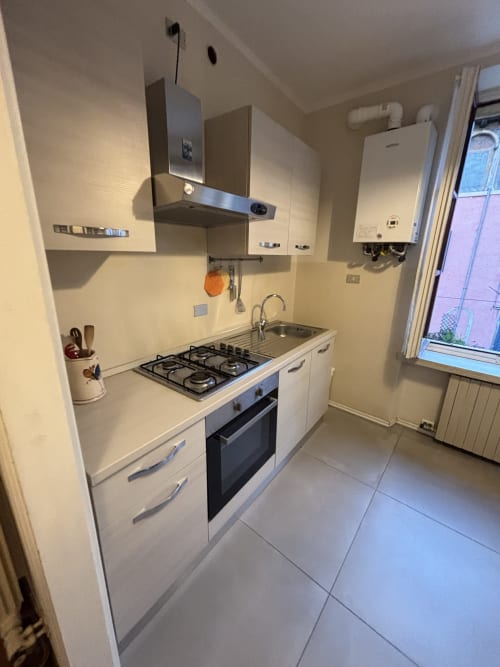 Cucina moderna compatta nell'appartamento Dimore Verona con fornello a gas, forno, lavello e mobili bianchi