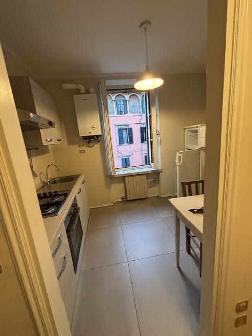 Cucina moderna nell'appartamento Dimore Verona, con mobili bianchi, fornello a gas, lampada a sospensione e vista città