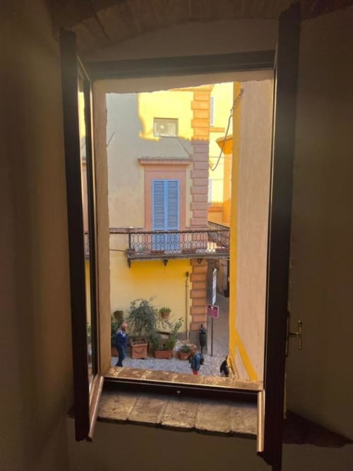 Ingresso aperto della Residenza San Jacopo che rivela la colorata corte di Spello con edifici gialli e piante in vaso